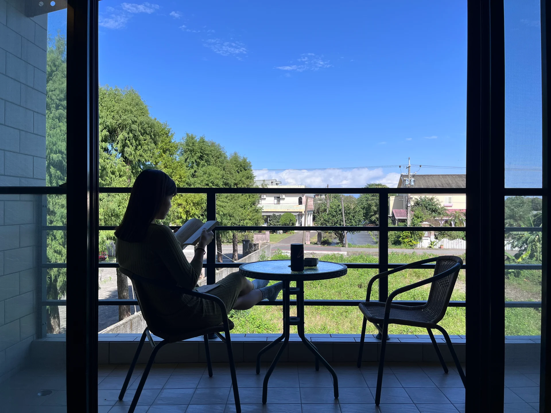 Jeany 坐在窗邊讀書，窗外是藍天、樹木與街景